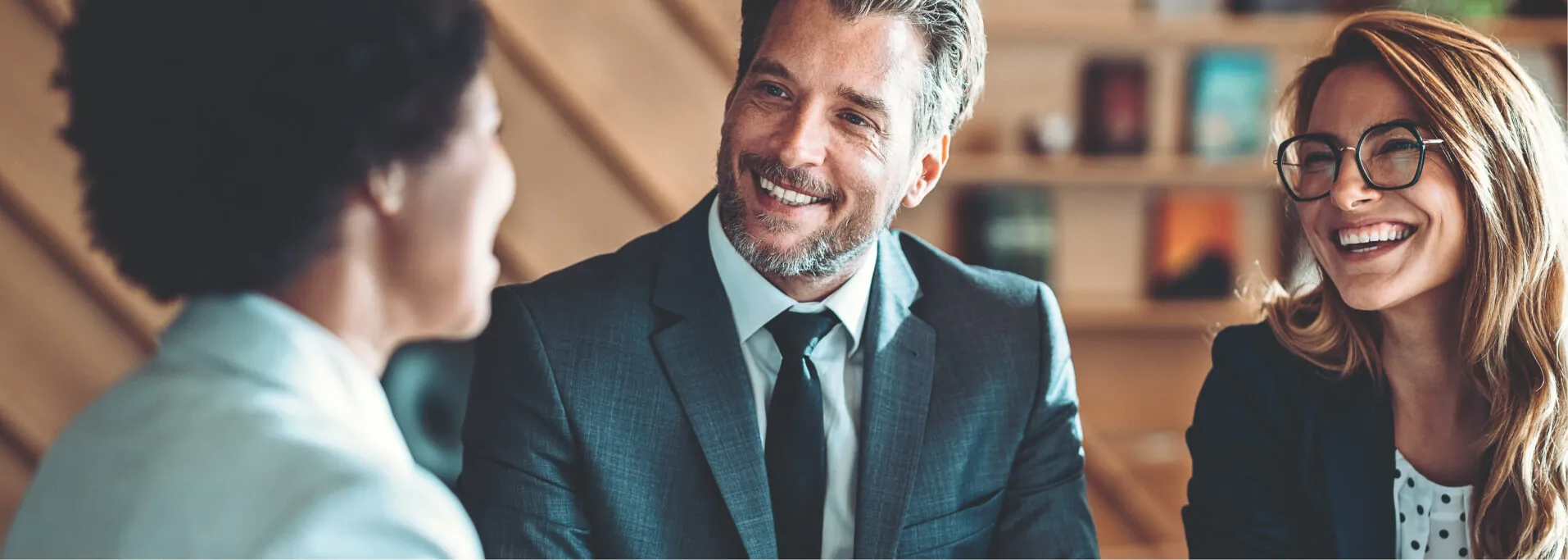 Drei lächelnde Personen unterhalten sich im Businessoutfit.